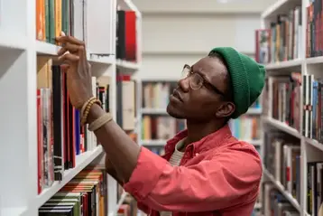 Independent author browsing reference titles on a library shelf
